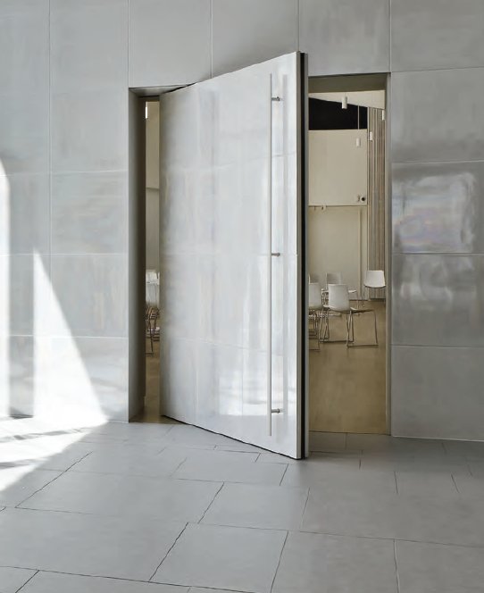 White lacquered pivot door set flush into a stone wall