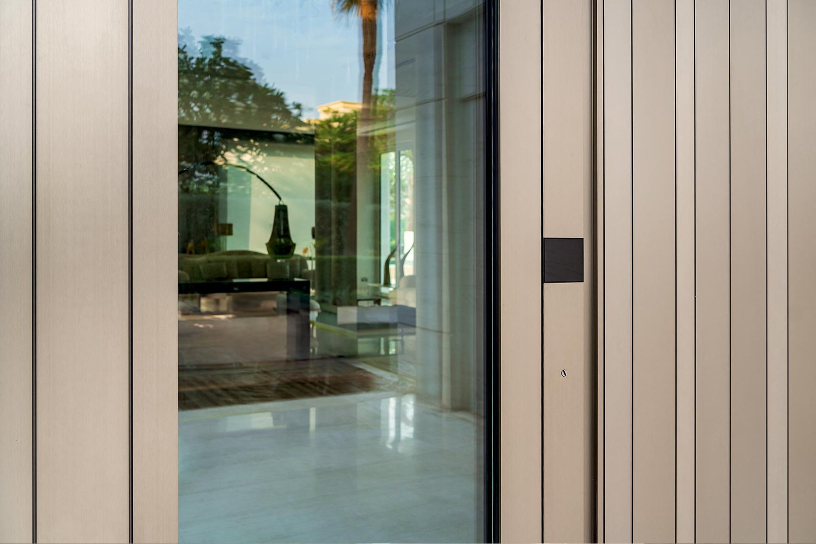 Glass pivot entry door between bronze metal panels