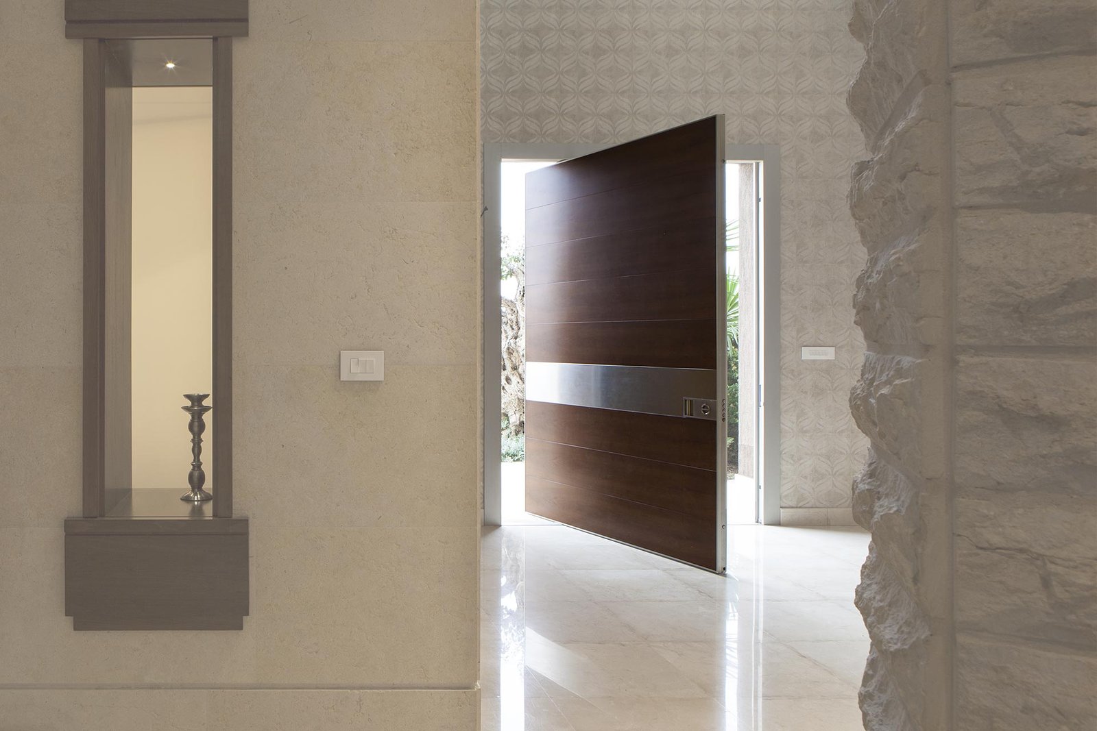 Walnut pivot entry door with a stainless band in a stone foyer