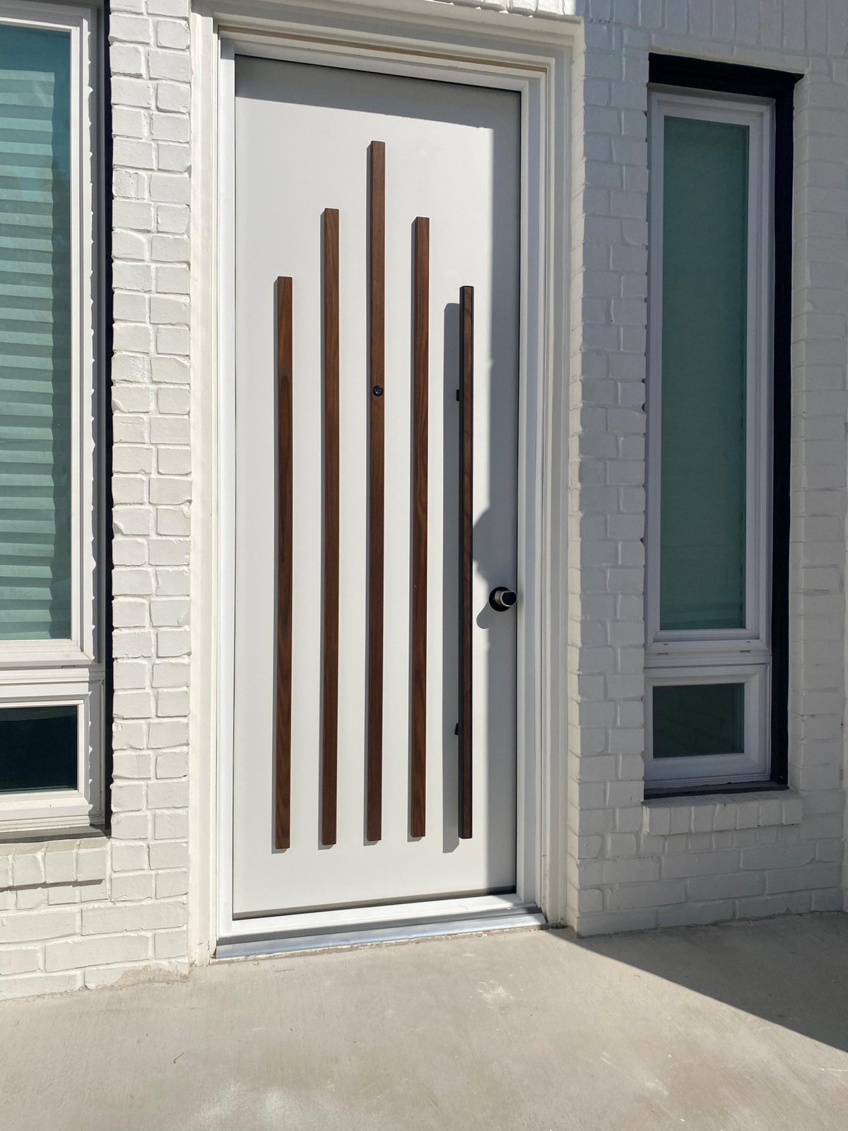 White entry door with walnut slat pulls between brick piers