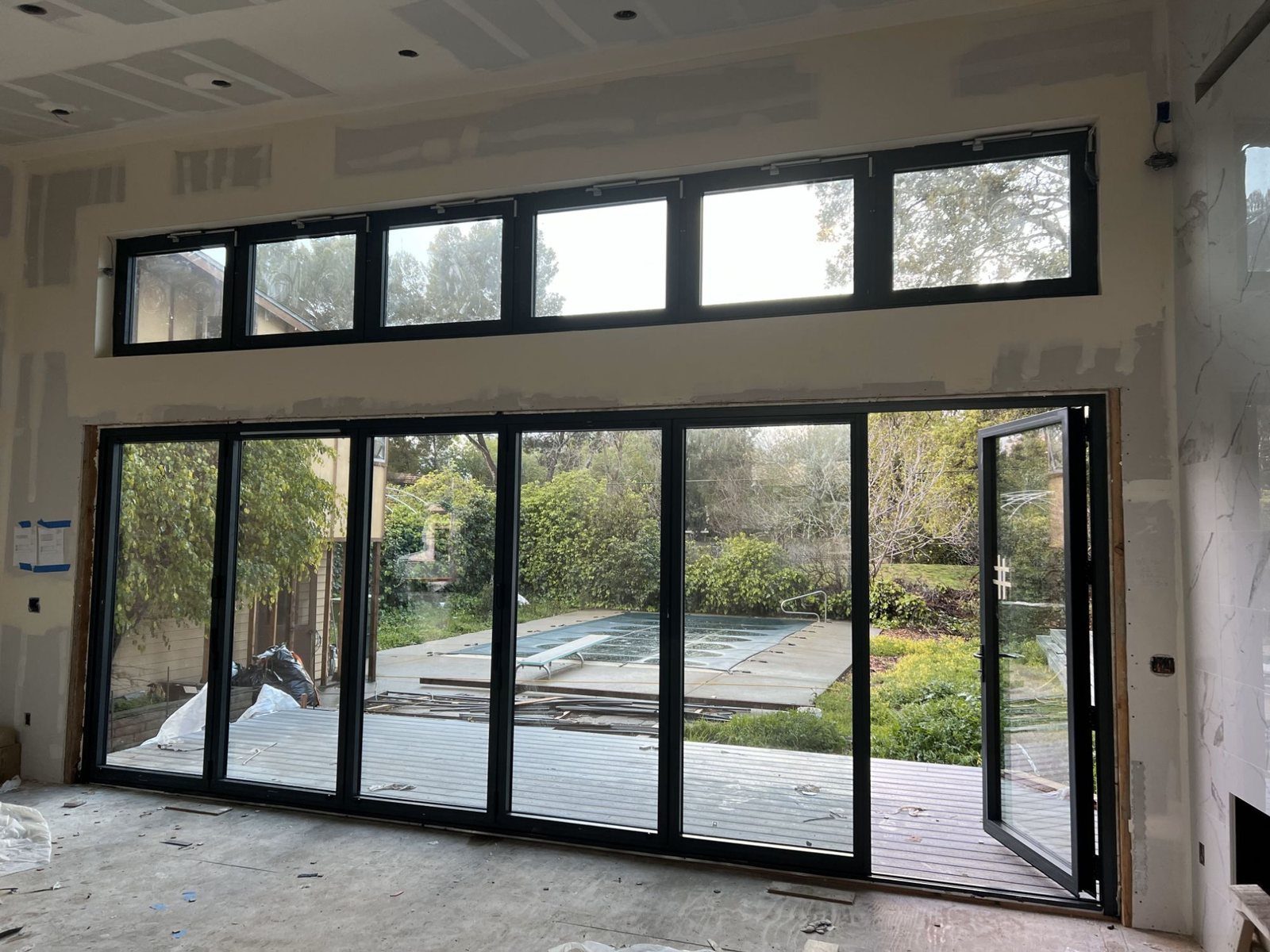 Six-panel black bifold door with awning clerestories opening to the pool
