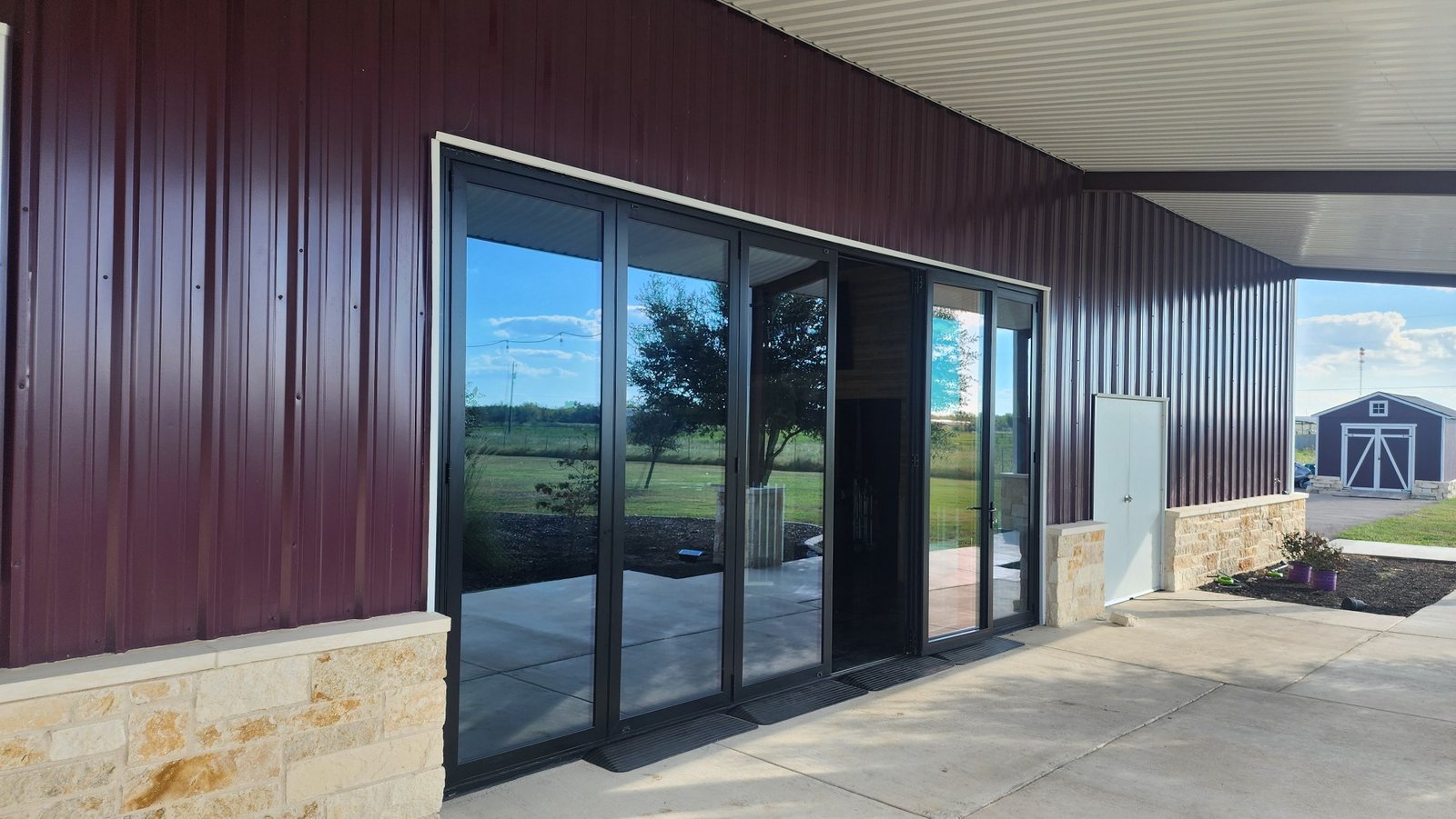 Black bifold doors folded open on a red steel building