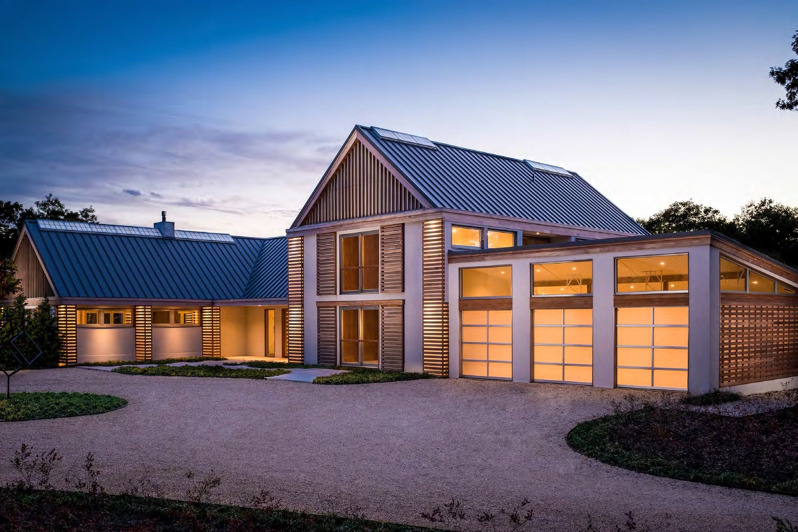 Barn-style home with full-view glass garage doors at dusk