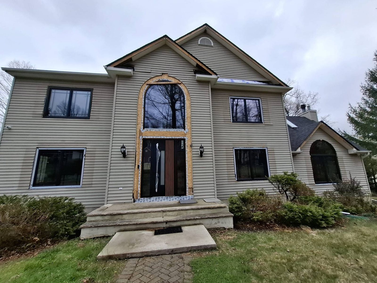 Colonial home refitted with black uPVC windows, an arched transom and a slatted entry door