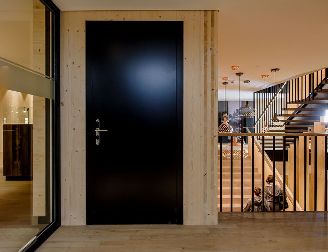 Flush black hotel door beside a timber stair hall