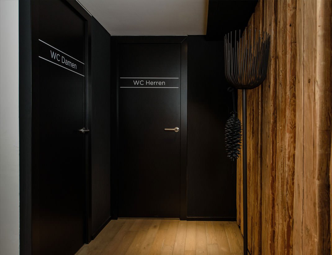Flush black restroom doors along a reclaimed-timber wall