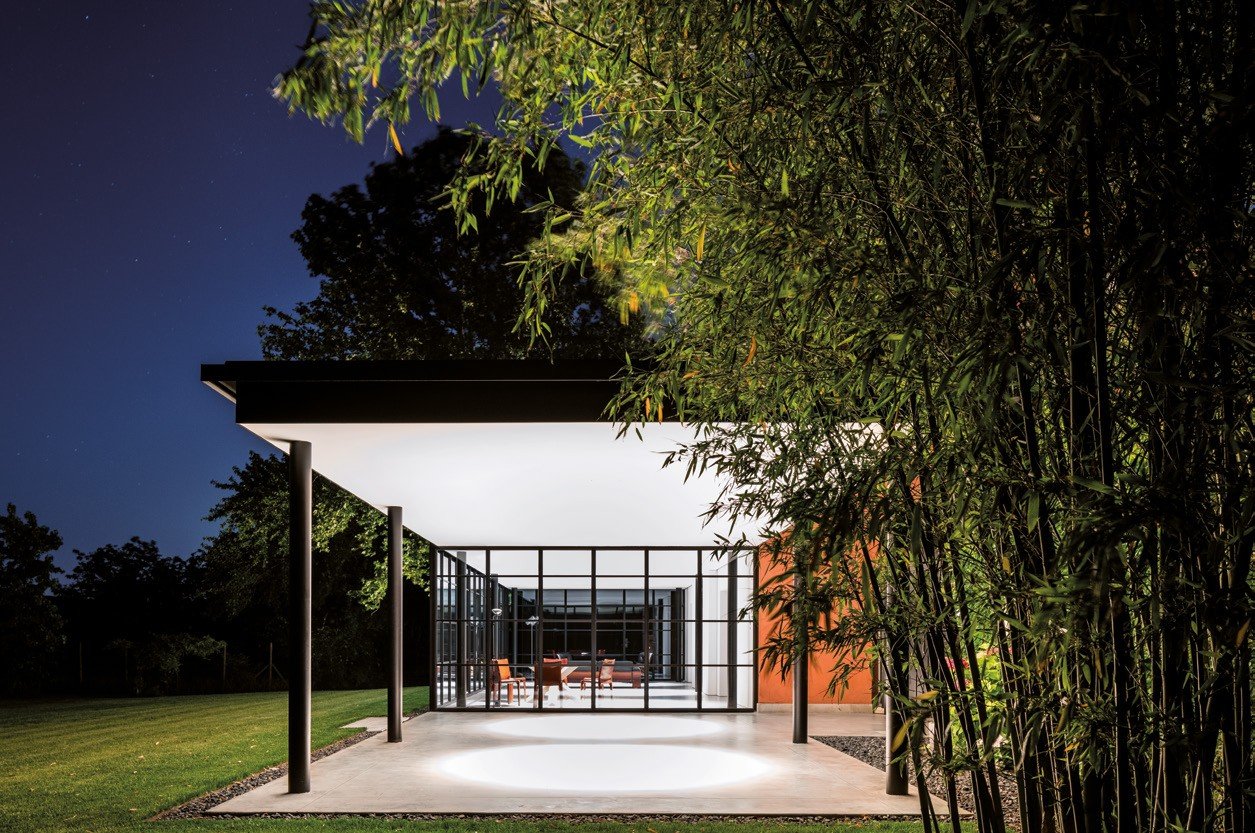Steel-and-glass pavilion lit at night among bamboo