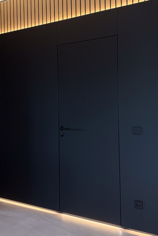 Flush black door set into a dark wall beneath a lit slat cornice